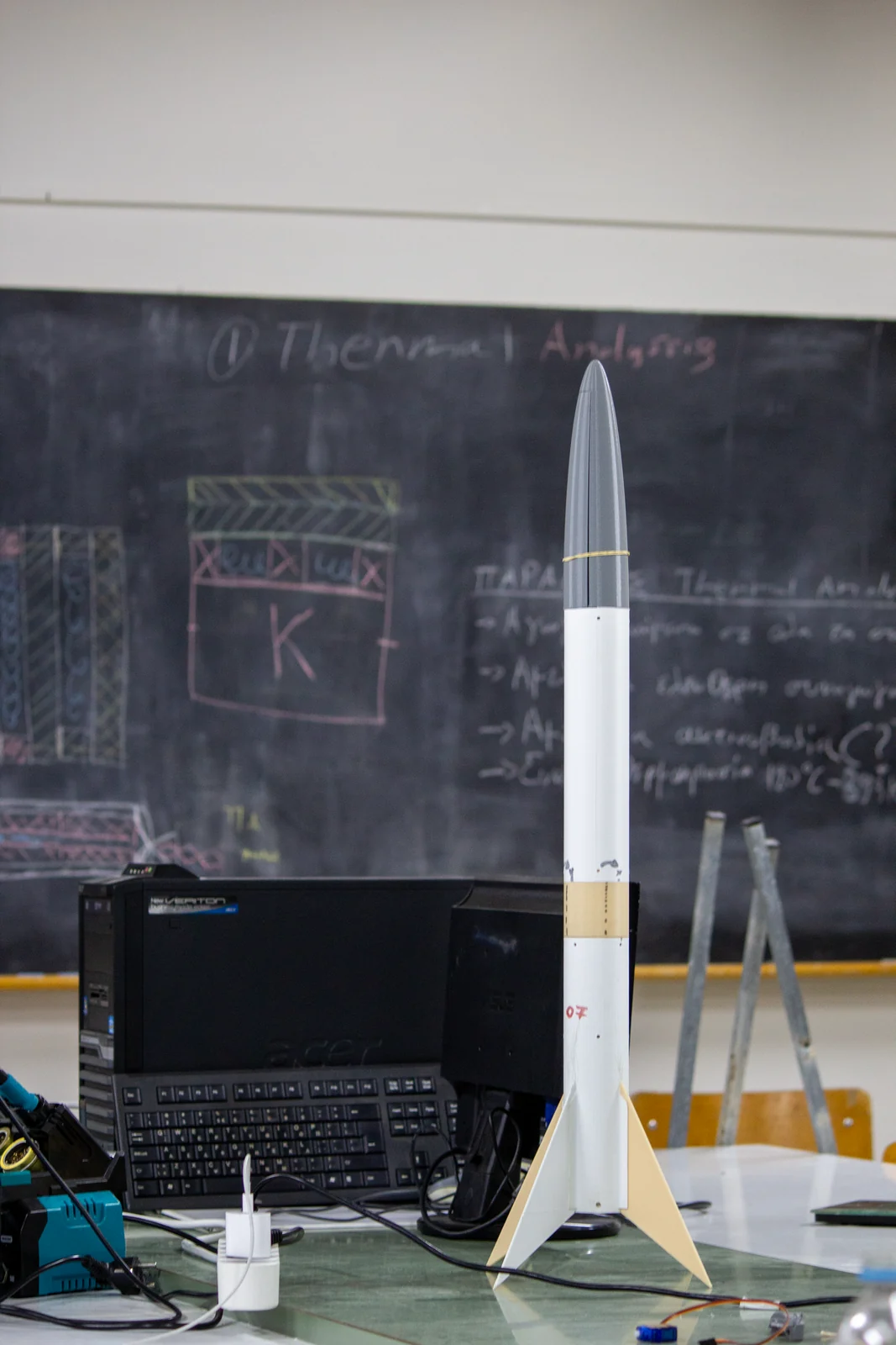 A SARISSA prototype rocket standing on the workshop bench beside a computer