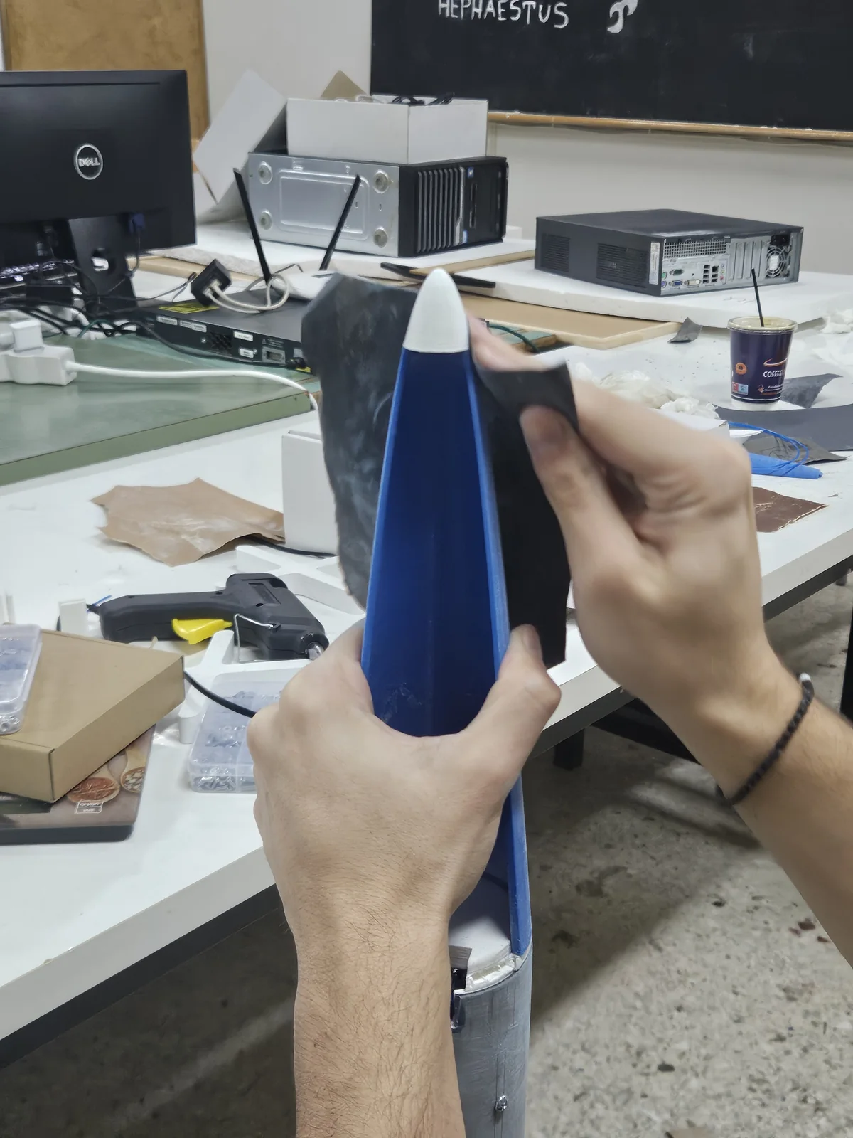 Work on a blue rocket nose cone on the HEPHAESTUS workshop bench