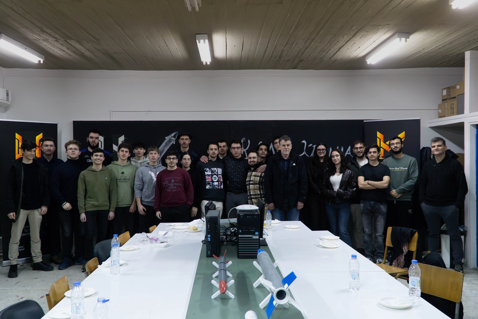 A HEPHAESTUS group photograph in the workshop, with prototype rockets on the bench